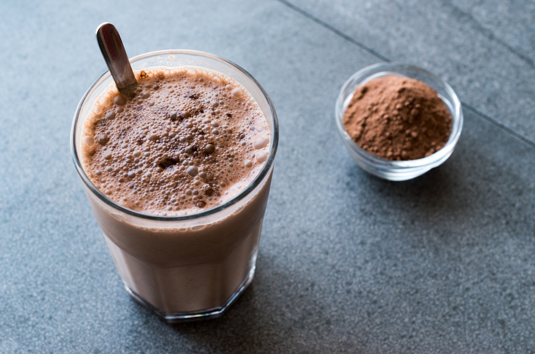 Golden Cocoa Shake In Glass With Spoon And Bowl Of Cocoa Powder
