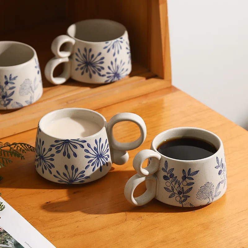 Cup Of Organic Coffee In 2 Loop Handled Ceramic Mug With Blue Nature Pattern Along With Dandelion Pattern Cup Of Milk And Other Garden Inspired Pottery Cups