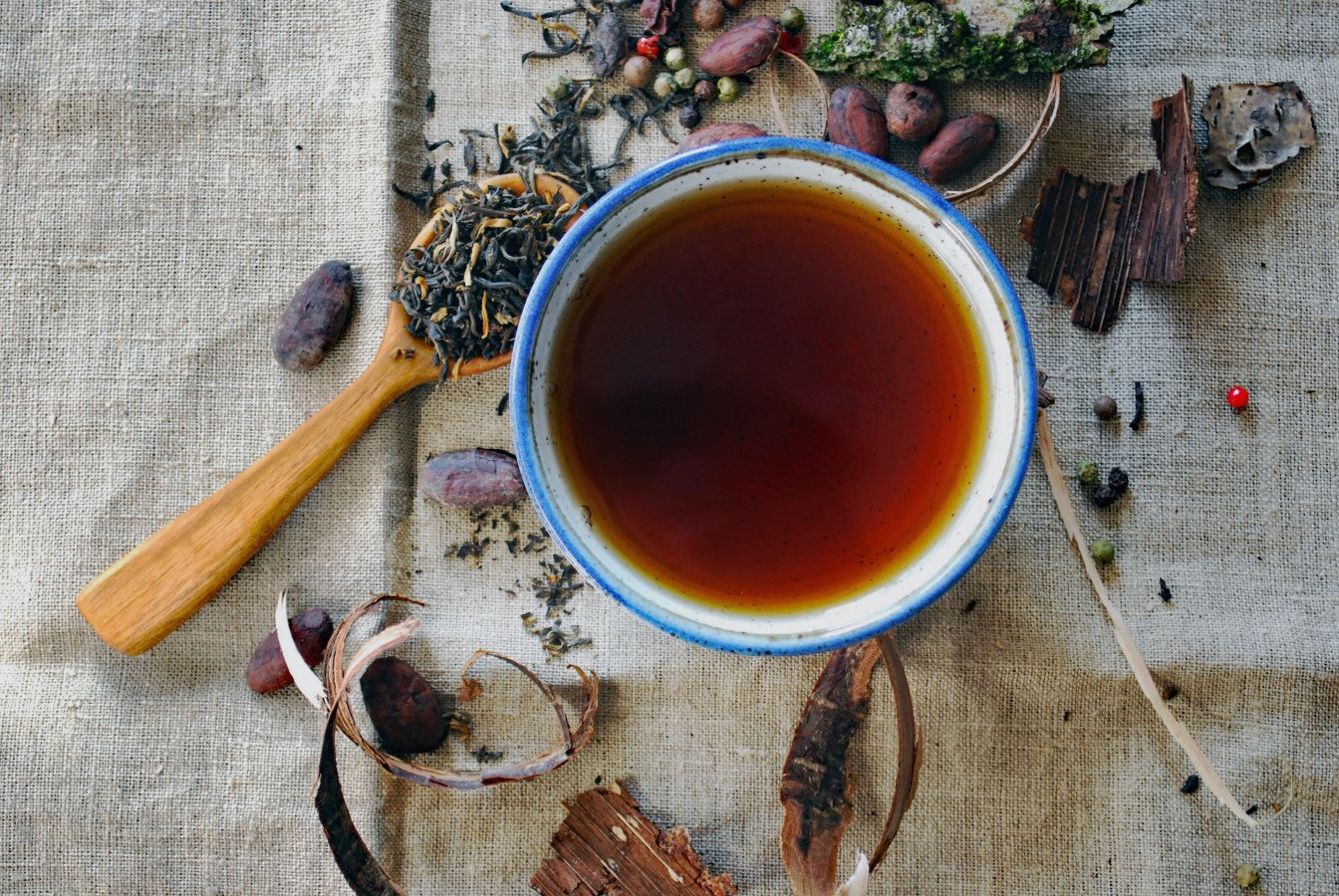 Blue Rimmed Cup Of Herbal Tea With Various Loose Tea Leaves And Nuts On Linen Cloth