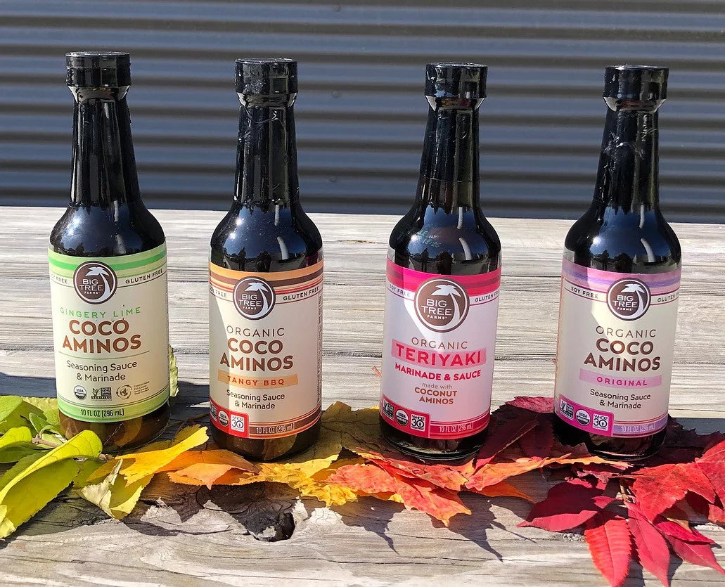 Four Bottles Of Big Tree Farms Organic Cooking Sauces Made With Coconut Aminos Sitting Outside On Autumn Leaves