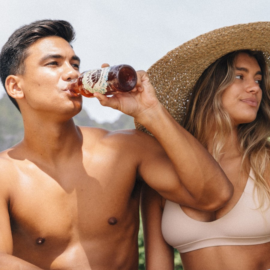 Couple At The Beach In Hawaii Man Drinking A Bottle Of Shaka Pineapple Mint Iced Tea For Refreshing Hydration