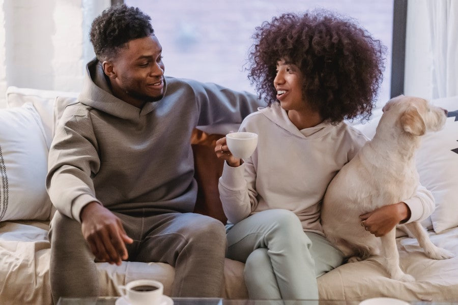 Couple Sitting On Couch Drinking Organic Coffee And Holding Dog