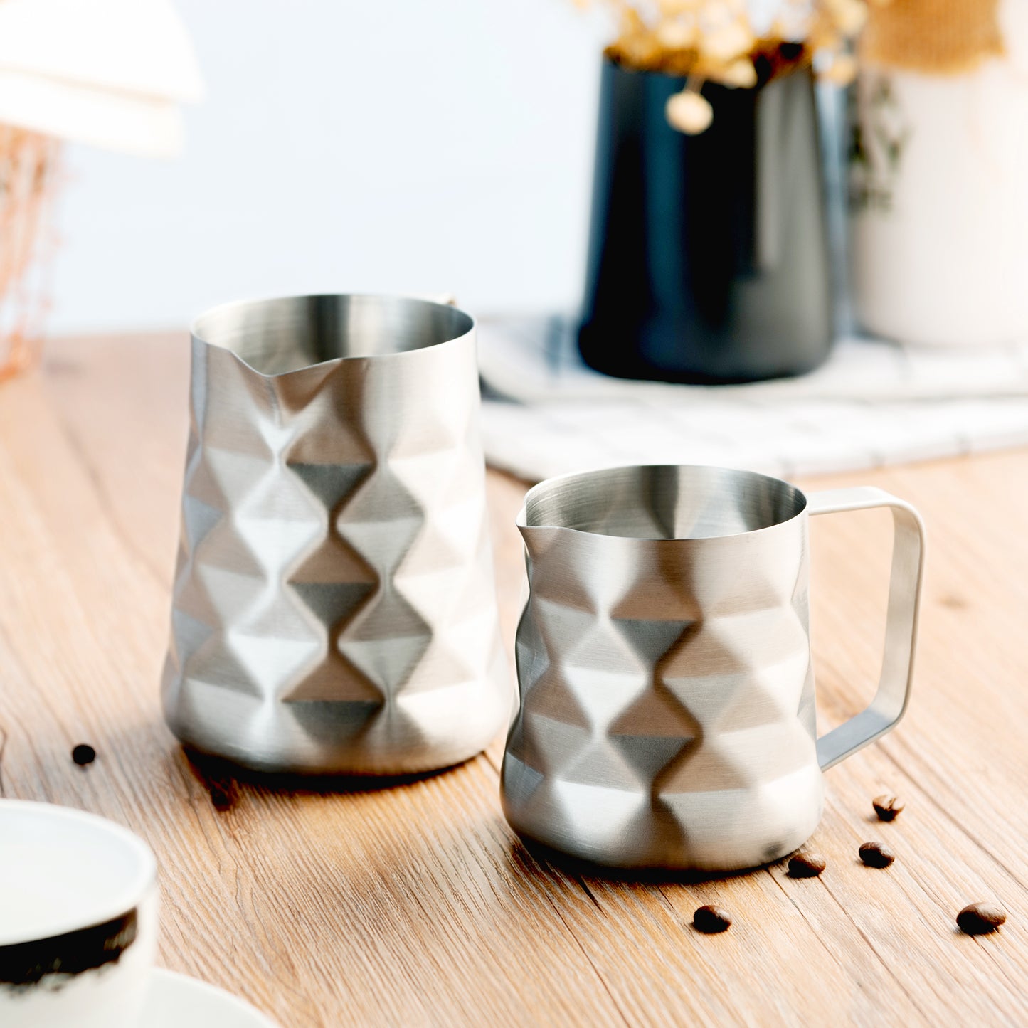 12oz And 20oz Stainless Steel Prismatic Frothing Pitchers On Table With Coffee Beans