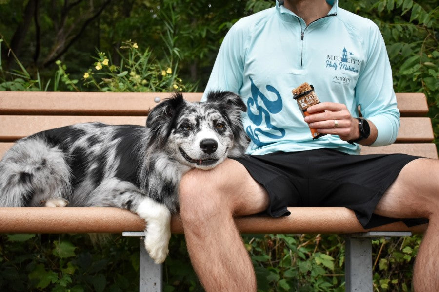 Happy Dog And Man On Bench Outdoors Eating A Kate's Mango Coconut Granola Bar