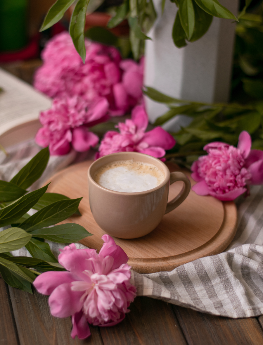 Mug With Frothed Milk Foamy Latte On Wooden Surface With Towel And Pink Flower Blooms