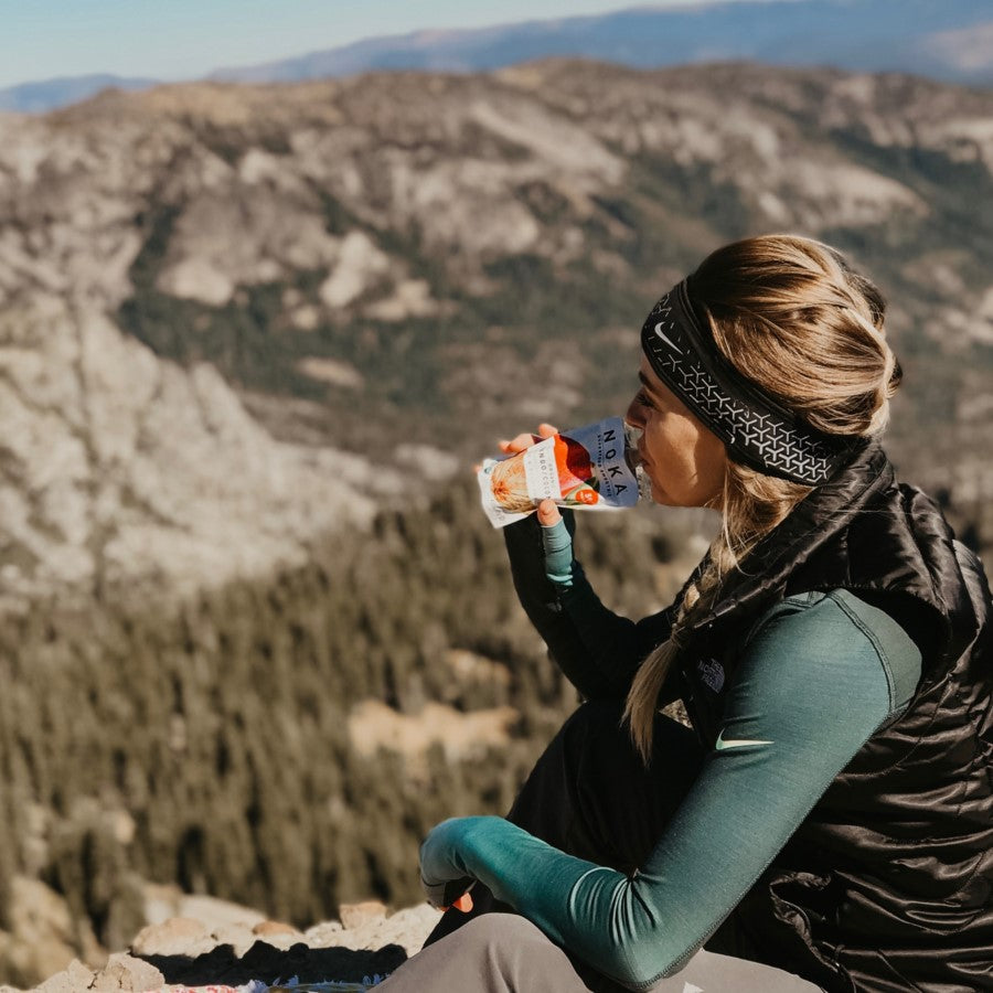 Woman On Hike Sitting On Mountain Taking A Break And Having An Organic Snack NOKA Coconut Mango Smoothie