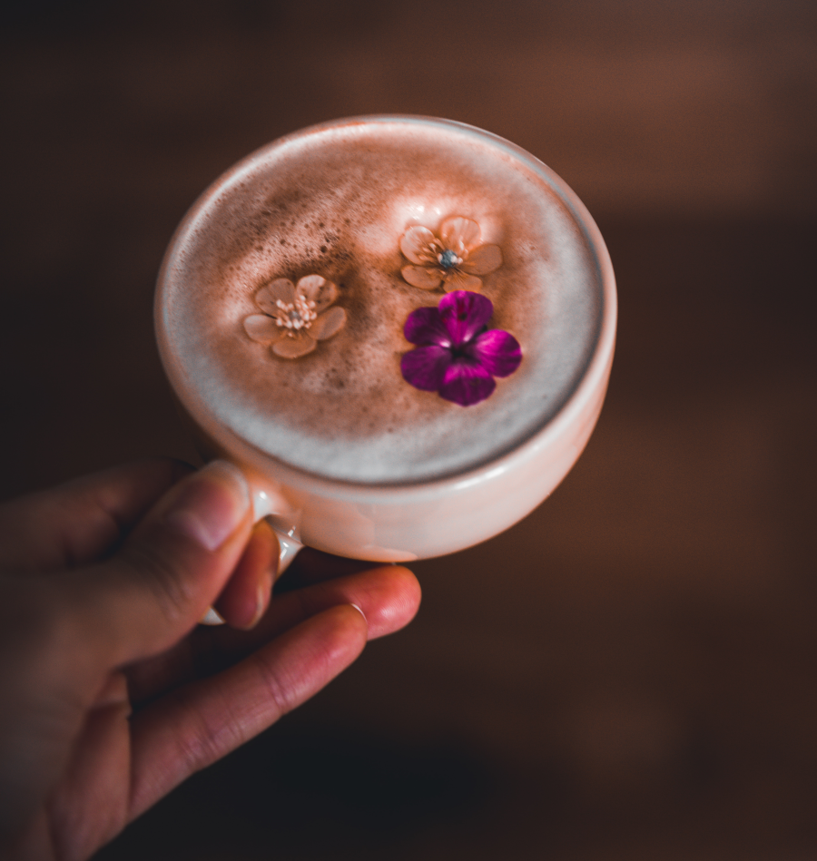 Hand Holding A Cup With Foamy Latte Topped With Three Flowers