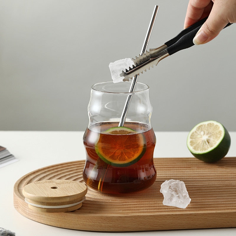 Adding Ice To Glass Of Tea In Wavy Glass Tumbler With Bamboo Lid