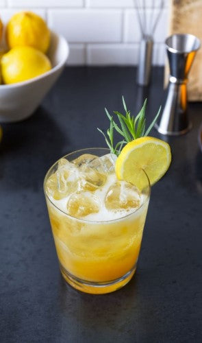 Turmeric tonic cocktail with lemon wedge and rosemary made from Rishi Chai Concentrate