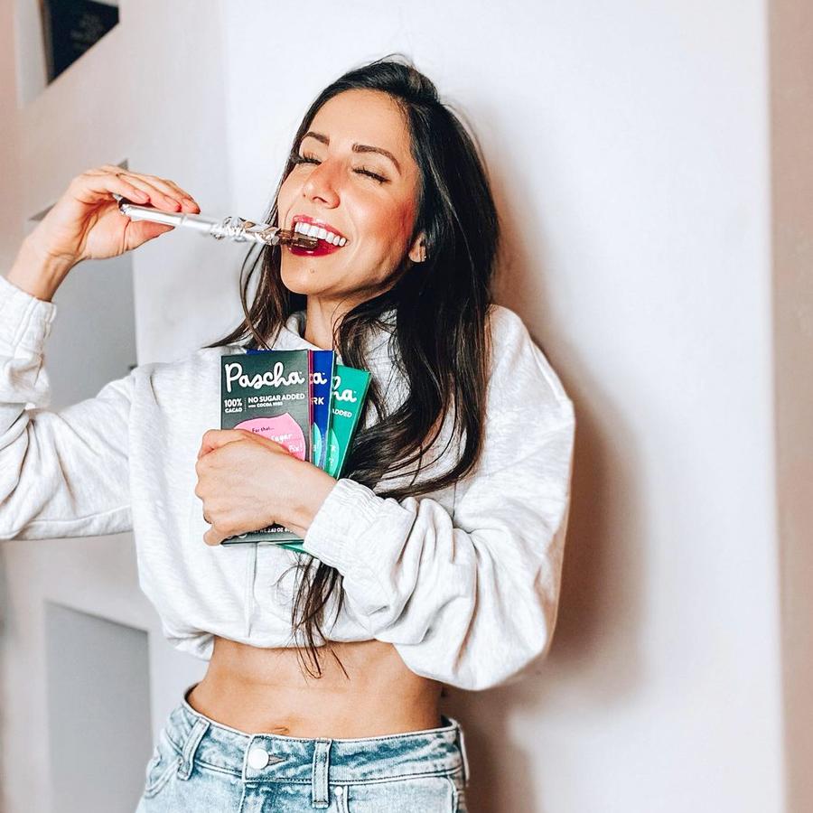 Woman Holding Several Organic Pascha Vegan Chocolate Bars And Eating One While Smiling