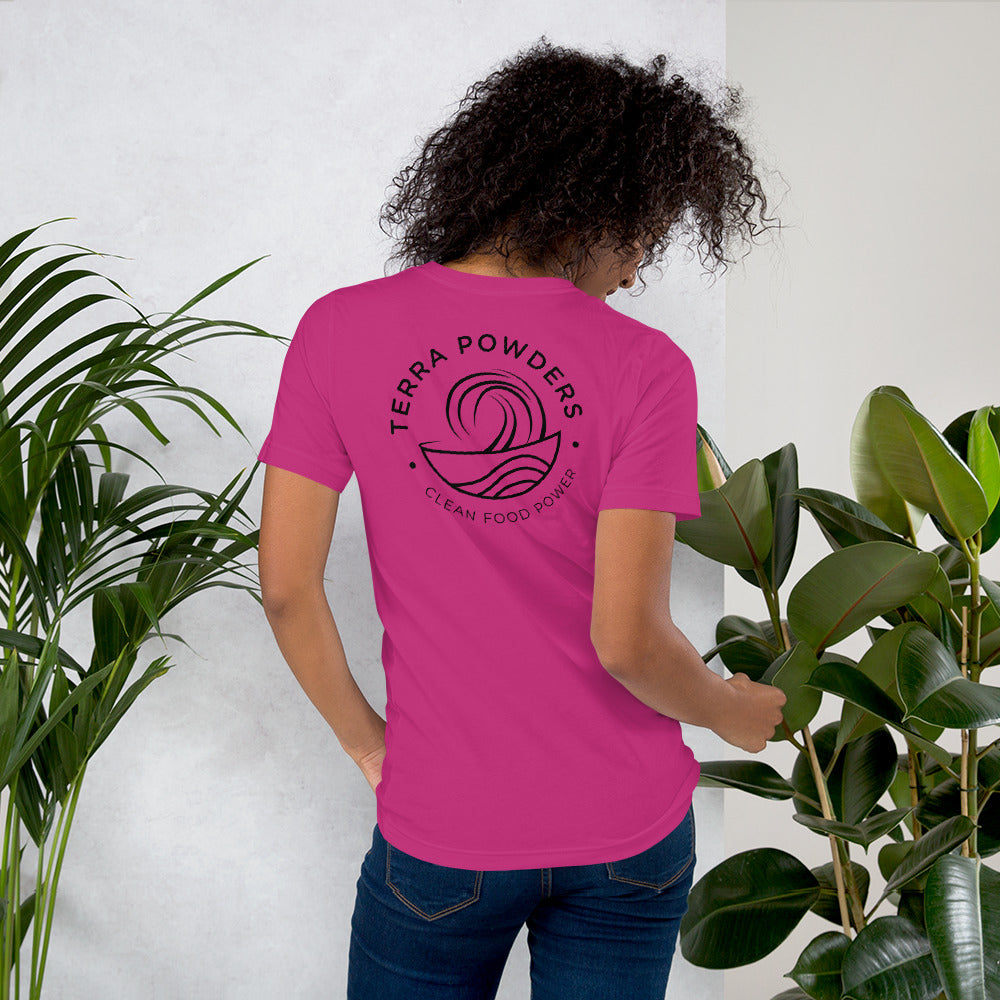 Woman Standing By Plants Wearing Shirt From Terra Powders Back Of Clean Food Powered Short Sleeve Shirt In Berry Pink With Terra Powders Logo