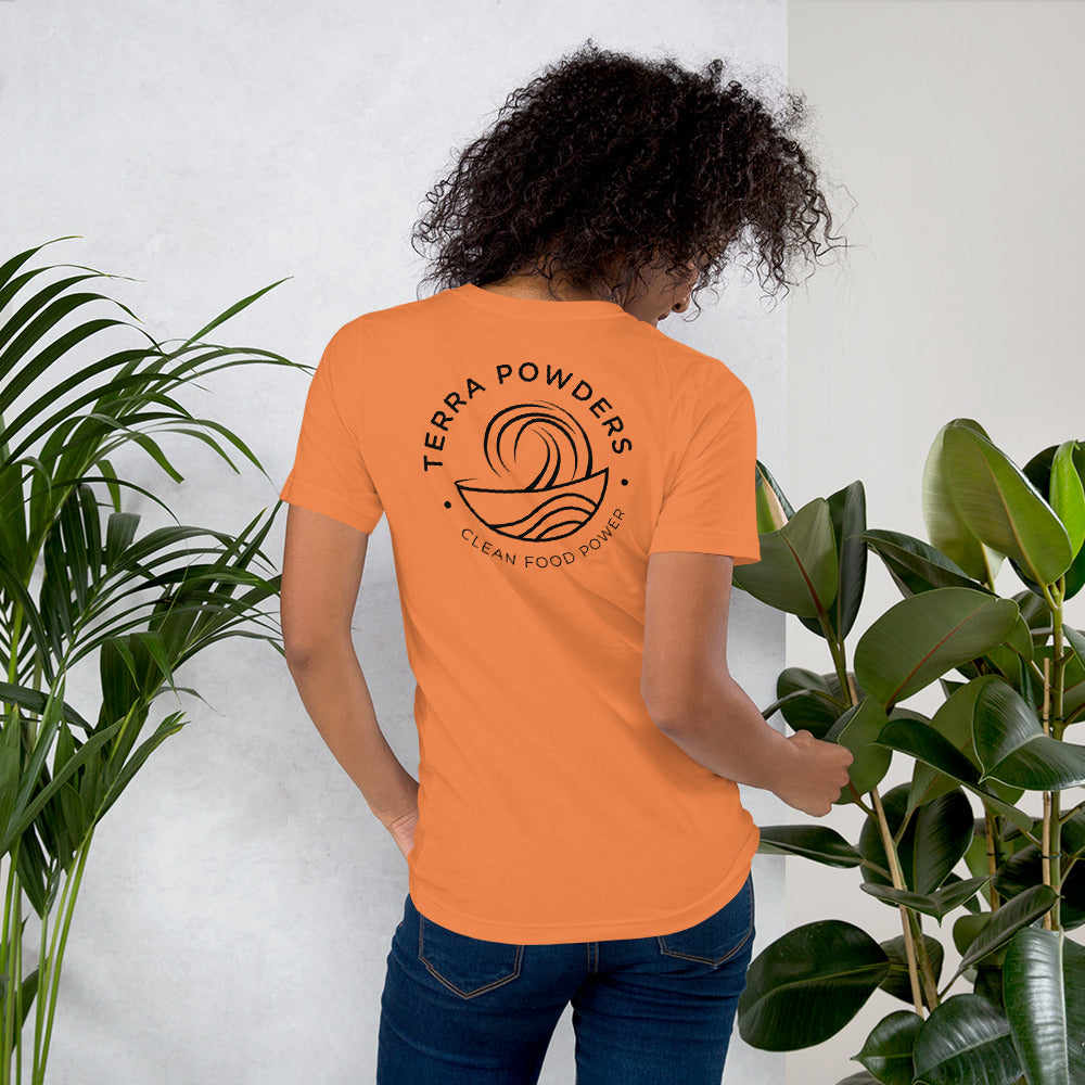 Woman Standing By Plants Wearing Shirt From Terra Powders Back Of Clean Food Powered Short Sleeve Shirt In Burnt Orange With Terra Powders Logo